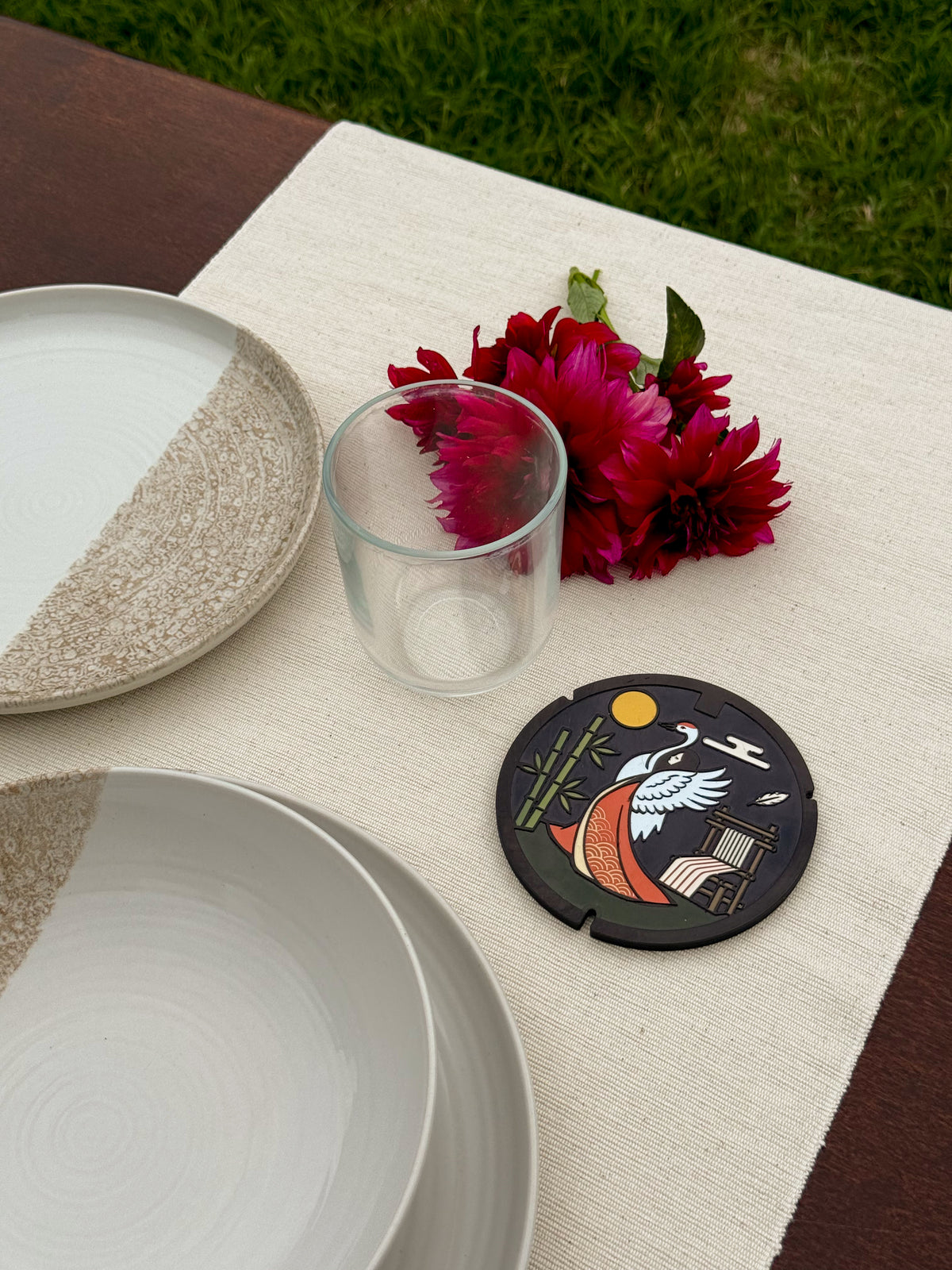 Tavola apparecchiata all'aperto con piatti in ceramica, fiori e un sottobicchiere ROJI con la gru